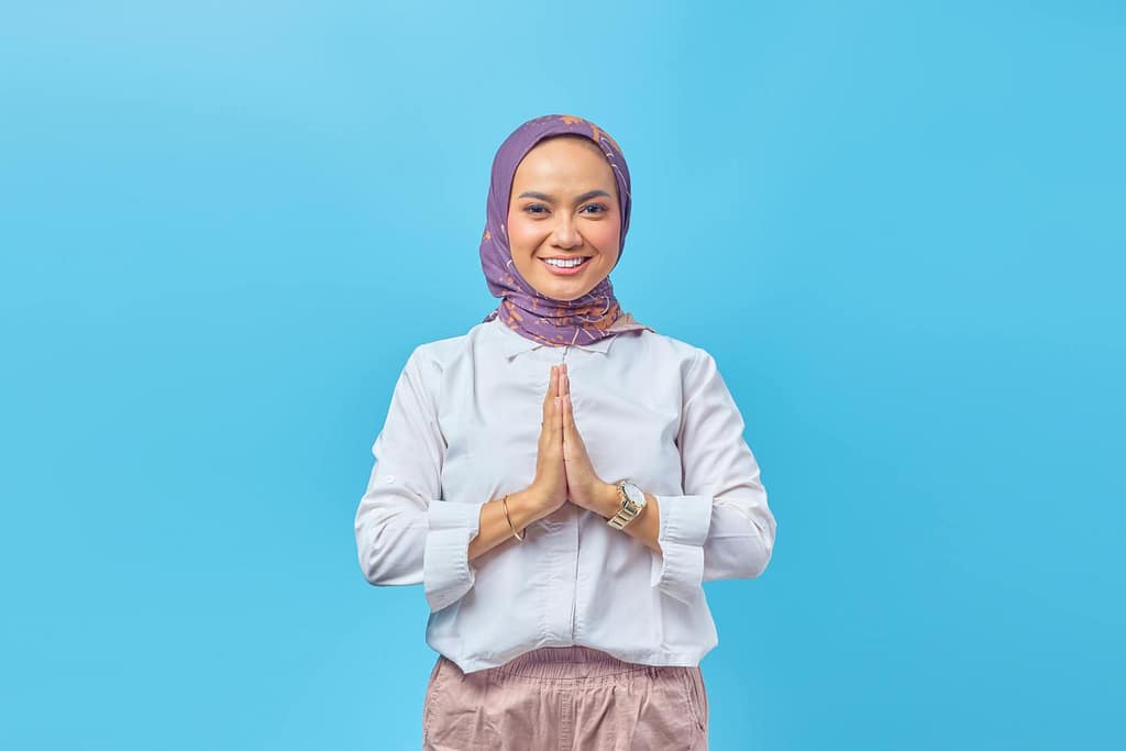 Portrait of a smiling Muslim woman in a studio setting with hands together.
