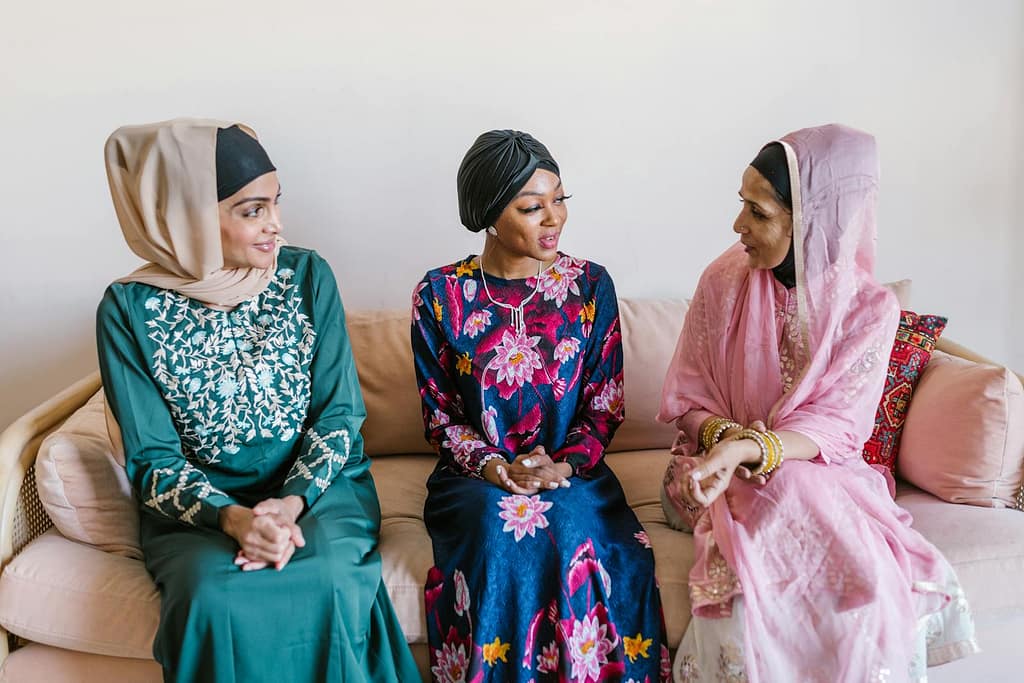 Three women wearing traditional Islamic attire engaged in conversation indoors.