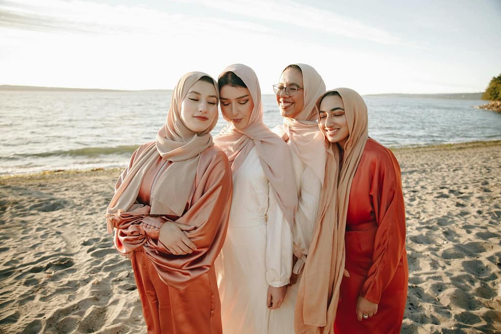 Four women in modest clothing enjoy a peaceful moment on the beach at sunset.